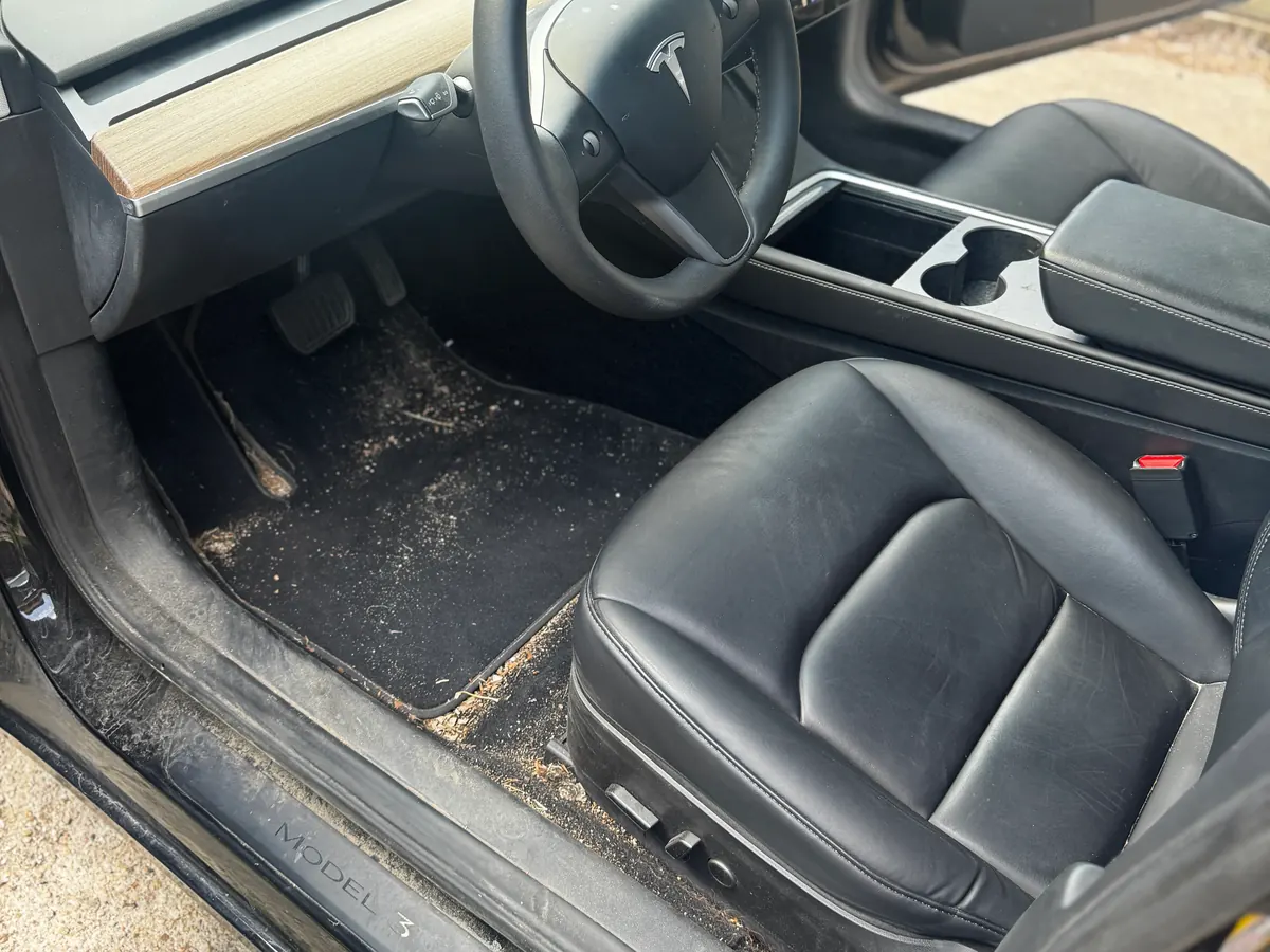 Tesla Model 3 driver footwell before detailing, carpet covered in dirt and debris