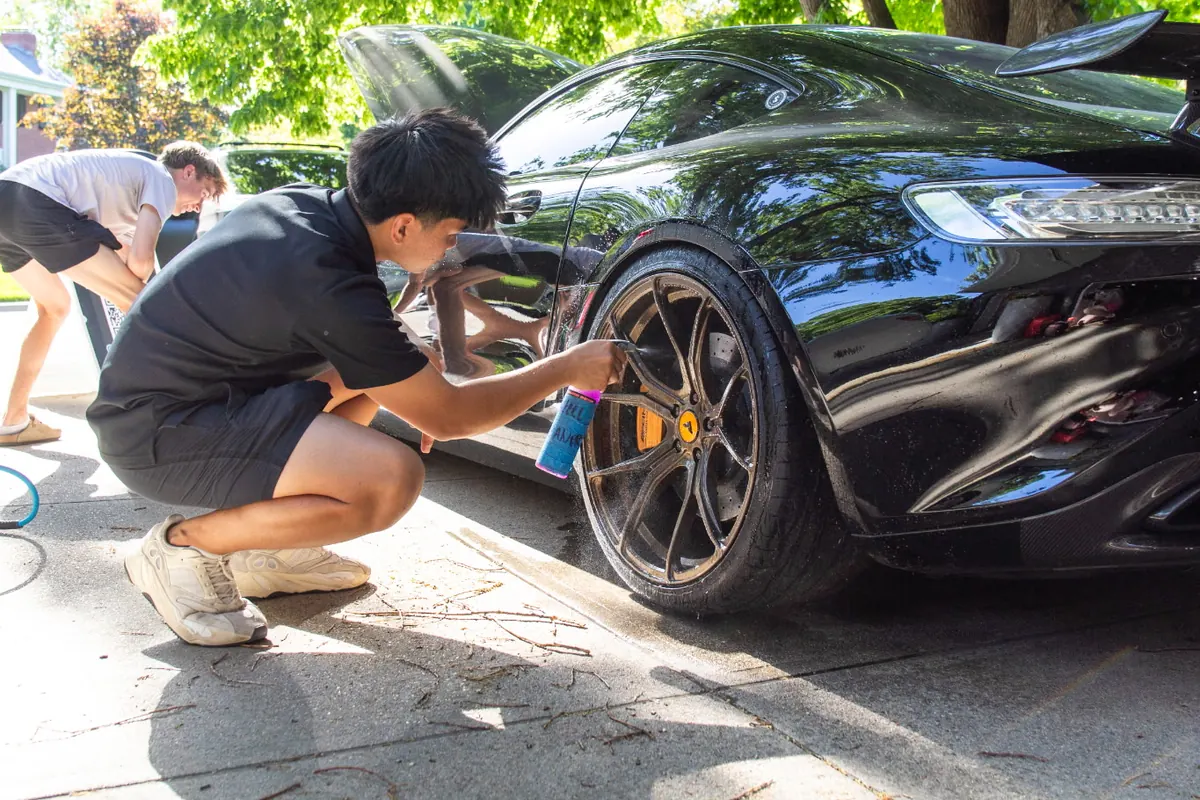 Signature detailer hand-cleaning the wheel of a black Mercedes-AMG GT
