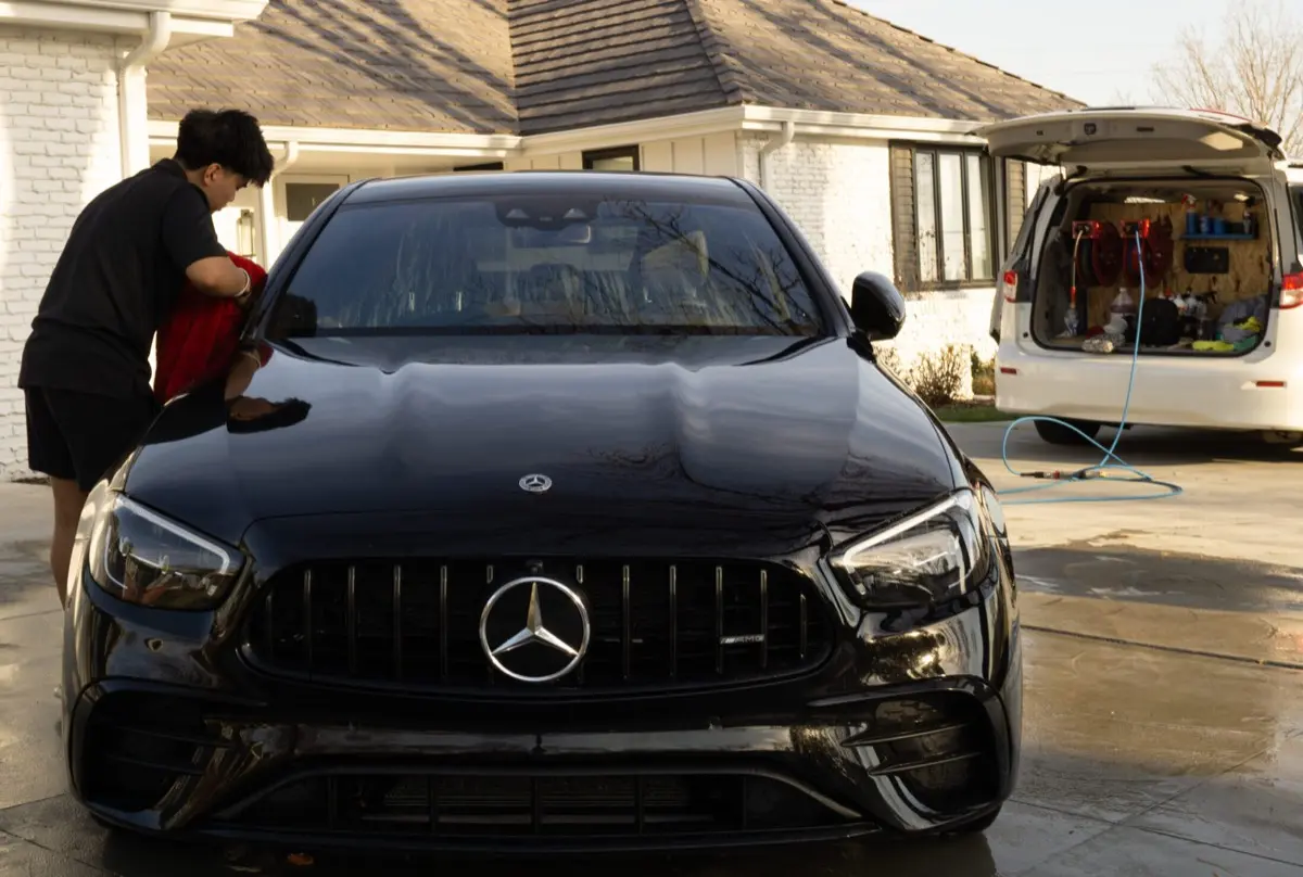 Detailer hand-washing a black Mercedes in a driveway
